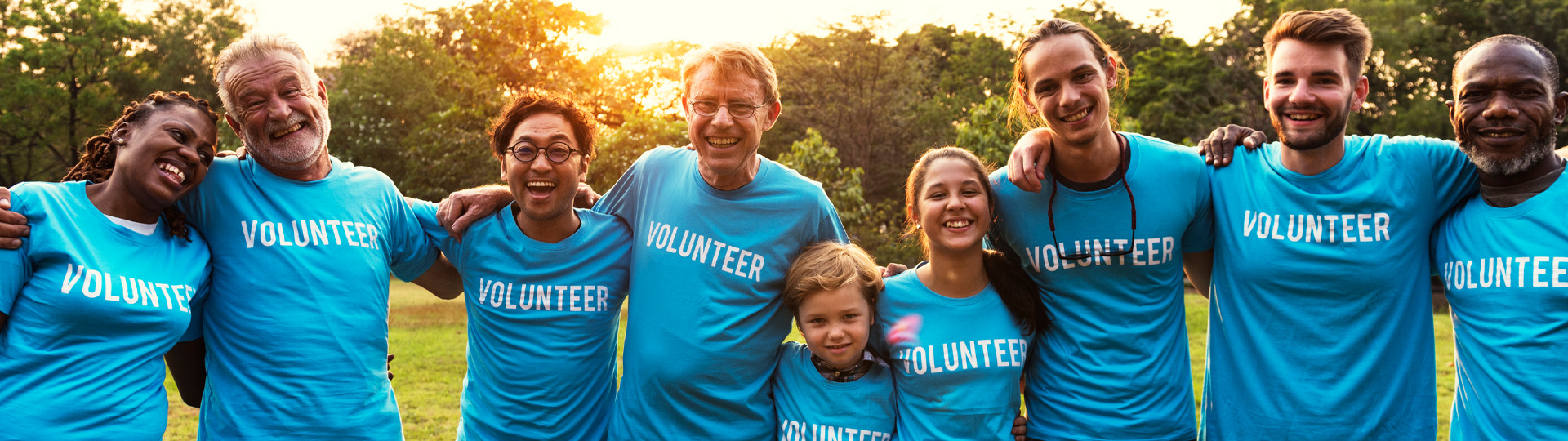 Volunteers hugging, wearing blue tshirts outdoors in s beatiful afternoon