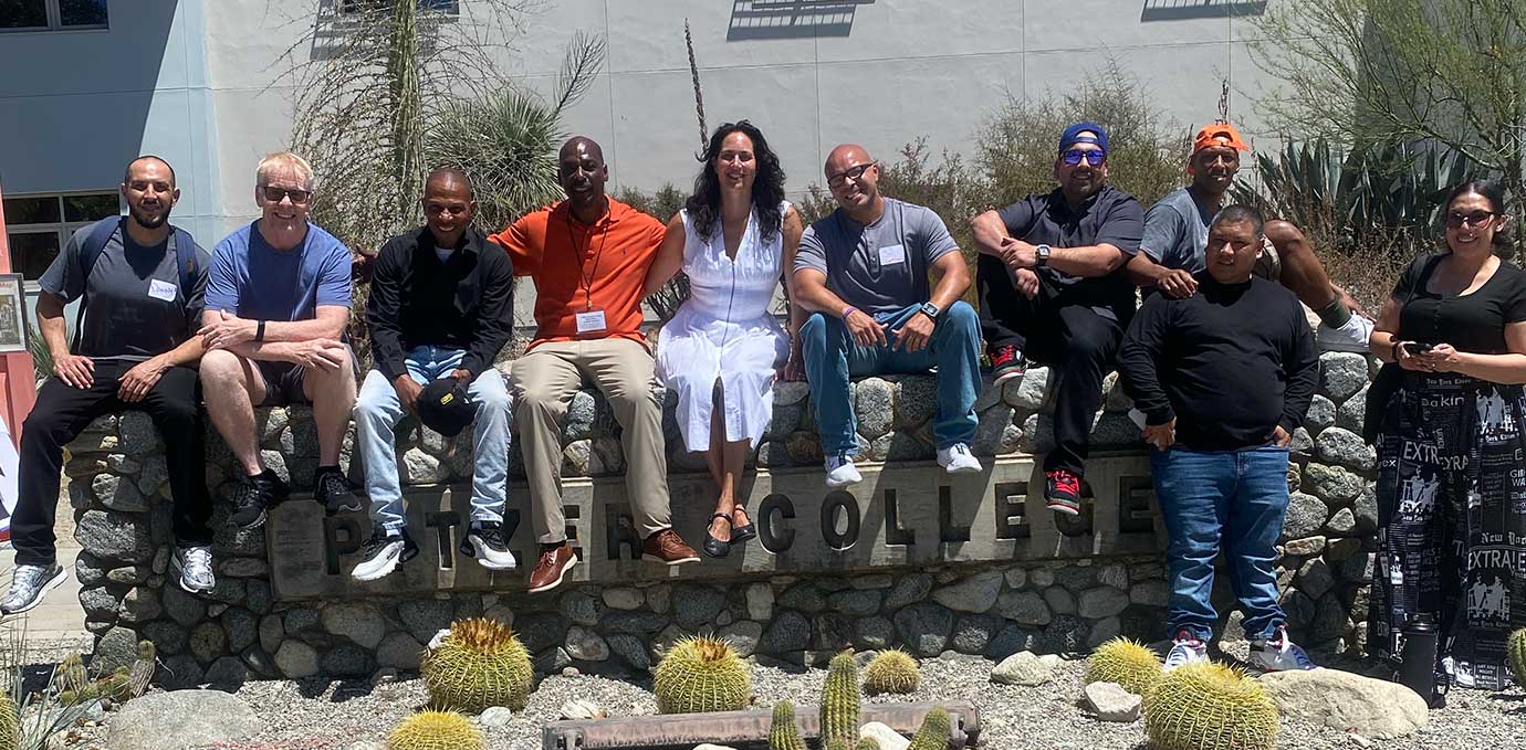 a group of students and professors pose sitting on top of the Pitzer College sign in front of Broad Center